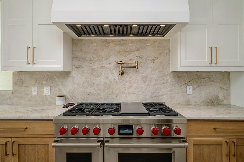 Professional gas range with full marble slab backsplash and brass pot filler
