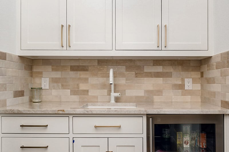 White kitchen sink under brass fixtures with tile backsplash and marble counter