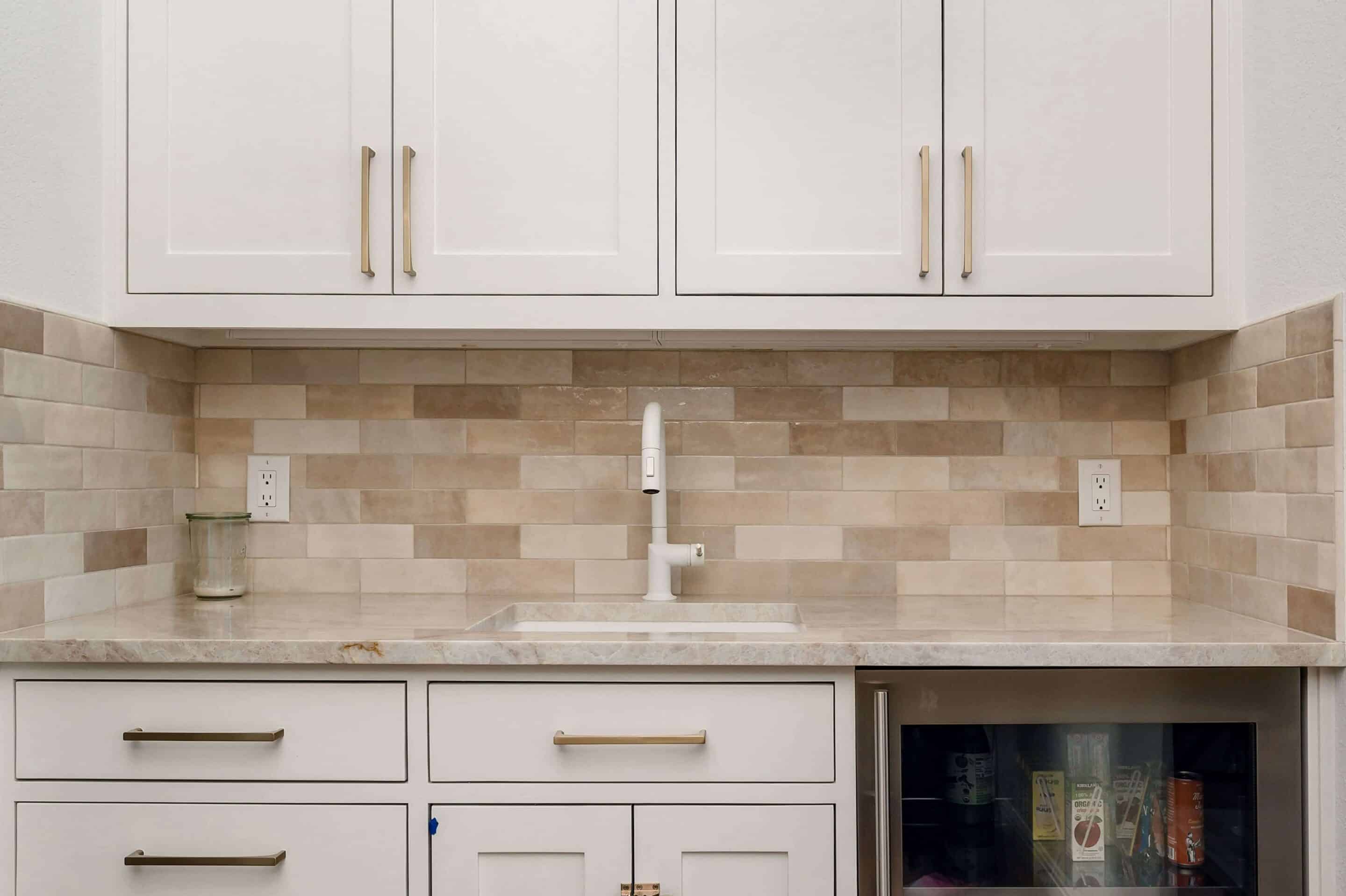 White kitchen sink under brass fixtures with tile backsplash and marble counter-tn